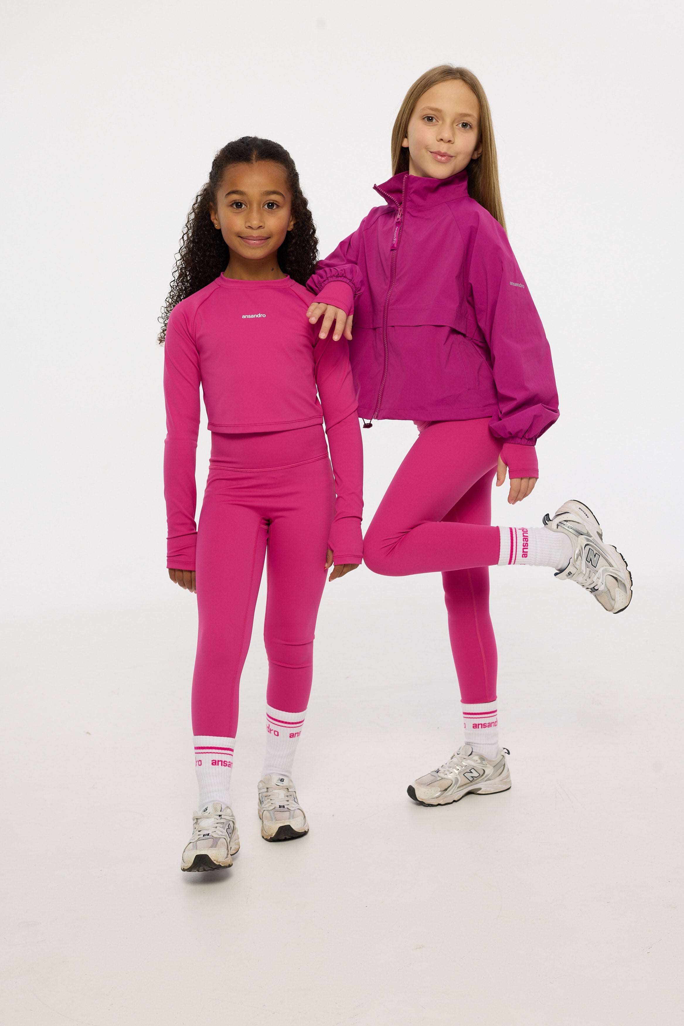 Two children wearing matching pink tracksuits on a white background