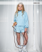 Person wearing a light blue tracksuit holding a jump rope against a white curtain background.
