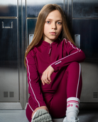 Young girl in a maroon tracksuit sitting against a metallic locker wall.