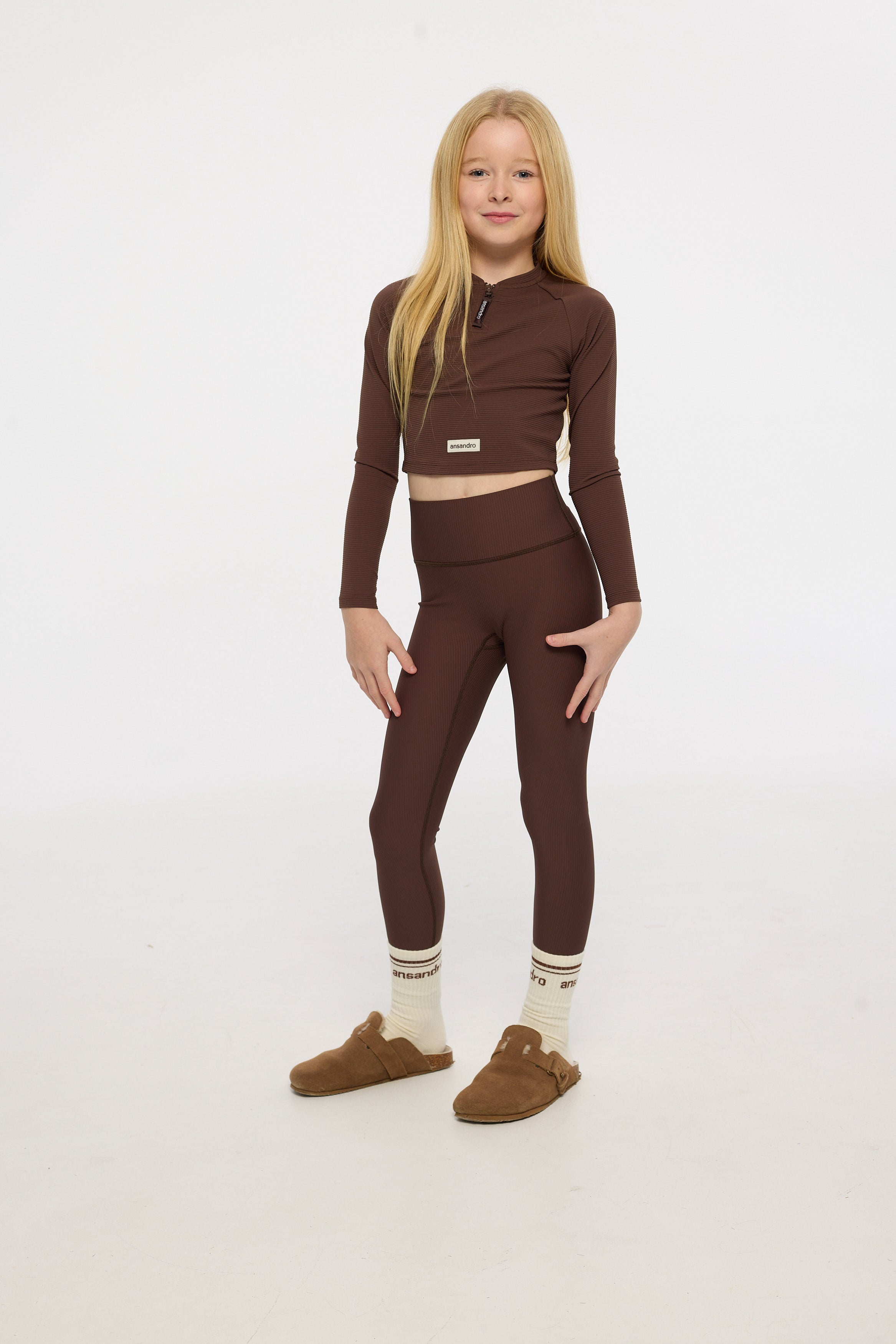 Young girl wearing a brown outfit with matching shoes and socks on a white background