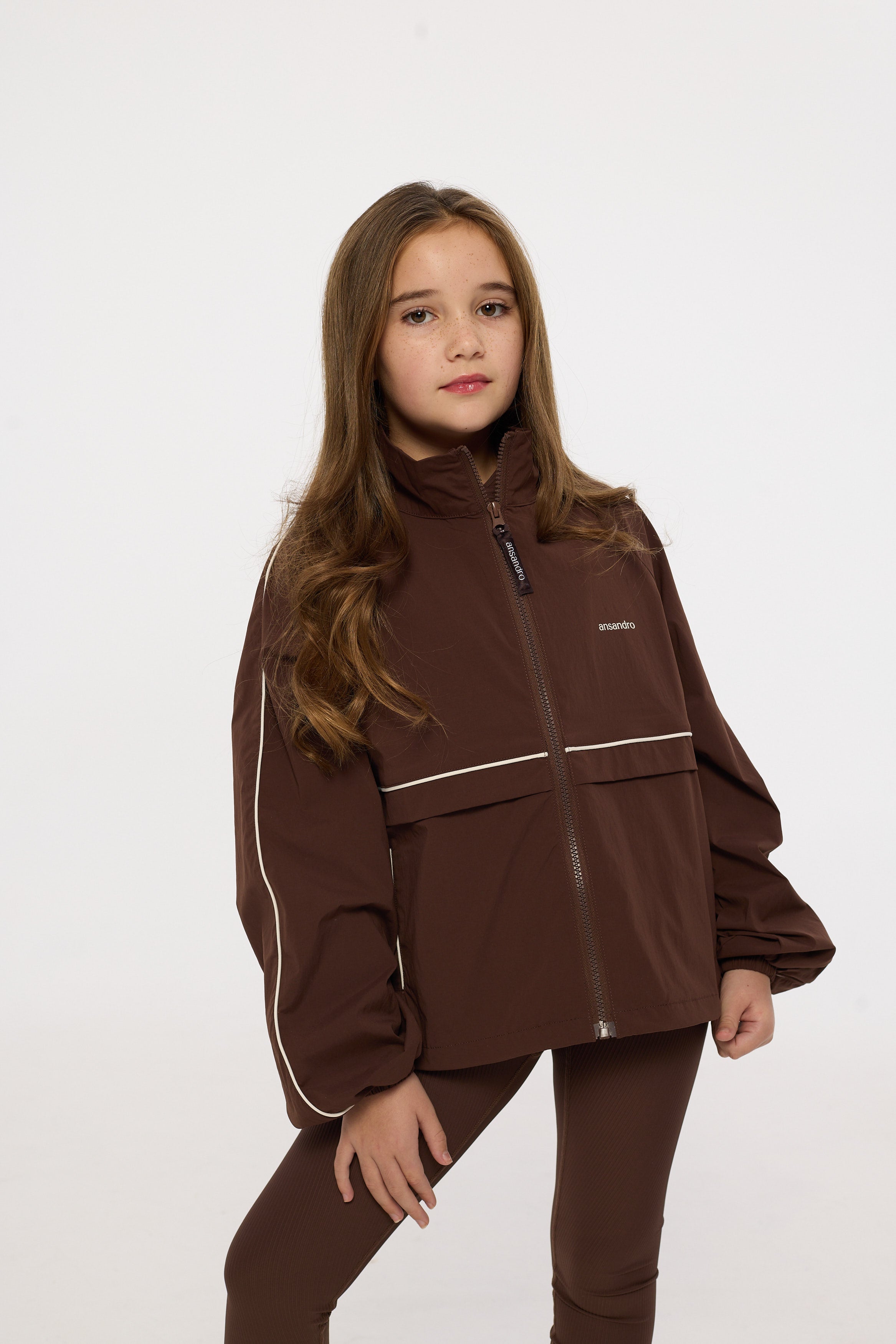Young girl wearing a brown jacket and pants on a white background