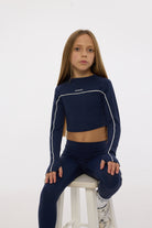 Girl wearing a navy blue athletic outfit with white accents on a white background