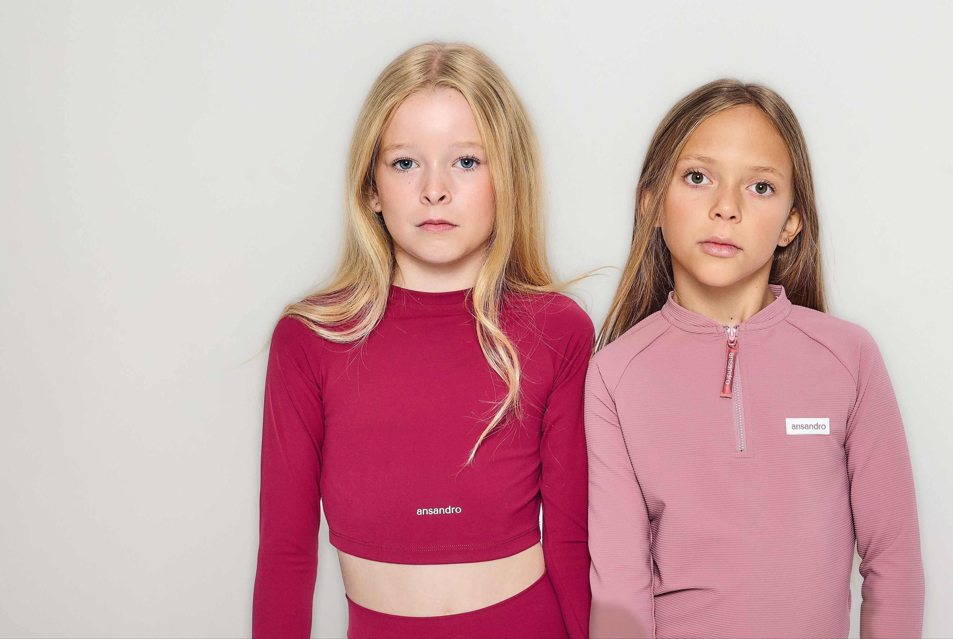 Two children wearing pink athletic outfits against a plain background
